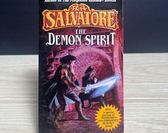 May include: A paperback book titled The Demon Spirit by R.A. Salvatore. The cover features a dark fantasy illustration of a figure holding a glowing blue sword in a stone chamber. A yellow starburst graphic on the cover mentions a special preview.