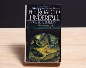 May include: A paperback book titled The Road to Underfall by Mike Jefferies, the first volume of Loremasters of Elundium. The cover features a dark archway framing a landscape with mountains, a full moon, and a structure under a night sky.