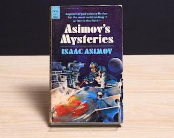 Może przedstawiać: Książka w miękkiej oprawie w stylu vintage zatytułowana Asimov's Mysteries autorstwa Isaaca Asimova. Ciemnoniebieska okładka zawiera ilustrację o tematyce kosmicznej przedstawiającą astronautę w skafandrze pracującego przy metalowej konstrukcji z czerwonym laserem.