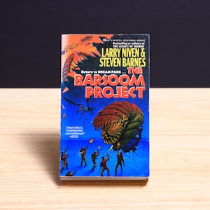 May include: A mass market paperback book titled The Barsoom Project by Larry Niven and Steven Barnes. The cover features a large, segmented, multi-colored creature, a group of figures holding glowing weapons, and a dark blue background.