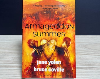 May include: A paperback book titled Armageddon Summer by Jane Yolen and Bruce Coville. The cover features a fiery orange and yellow background with silhouettes of two people standing back-to-back, separated by a glowing heart-shaped light.