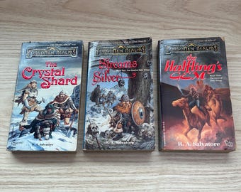 May include: Three mass-market paperback fantasy novels from the Forgotten Realms series by R.A. Salvatore, titled The Crystal Shard, Streams of Silver, and The Halfling's Gem, featuring colorful illustrated covers with characters and landscapes.