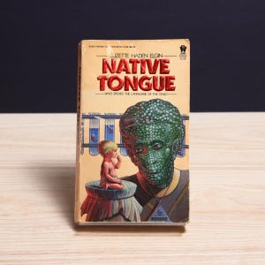 May include: A mass-market paperback book titled Native Tongue by Suzette Haden Elgin. The cover features a green, reptilian-skinned humanoid figure, a small child sitting on a draped pedestal, and test tubes containing small organisms in the background.