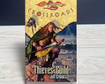 Könnte beinhalten: Ein Taschenbuch mit dem Titel Dragonlance Crossroads: The Thieves' Guild von Jeff Crook. Das Cover zeigt eine Fantasy-Illustration einer langhaarigen Figur in einem grünen Umhang, die ein leuchtendes Schwert hält, mit einer Stadtansicht.