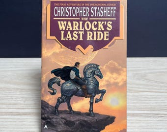 May include: A paperback book titled The Warlock's Last Ride by Christopher Stasheff. The cover features an illustration of a person in a dark cape riding a metallic, mechanical horse on a cliffside against a sunset sky with a large planet.