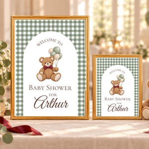 Puede incluir: Dos letreros con marco dorado que presentan un borde de cuadros vichy verde y blanco y un centro arqueado. Los letreros muestran un oso de peluche marrón con pajarita granate sosteniendo globos, con el texto: Welcome to Baby Shower for Arthur.