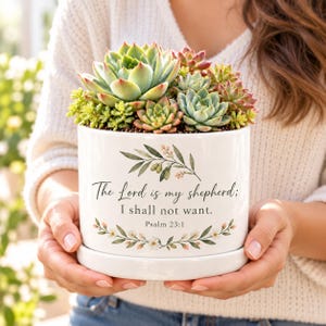 May include: A white ceramic planter with a matching saucer containing a variety of green and reddish succulents. The planter features a botanical illustration of olive branches and the text "The Lord is my shepherd; I shall not want. Psalm 23:1."