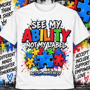 May include: A white t-shirt featuring a colorful graphic with the text "SEE MY ABILITY NOT MY LABEL" and "AUTISM AWARENESS" in a graffiti style. The design includes vibrant red, blue, yellow, and green puzzle pieces and paint splatters.