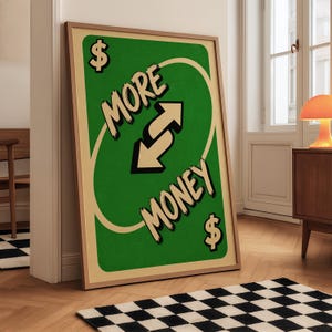 Puede incluir: Un cuadro rectangular enmarcado con fondo verde y borde color crema. El diseño imita una carta de juego con dos flechas opuestas en el centro, el texto MORE MONEY y signos de dólar en las esquinas superior izquierda e inferior derecha.