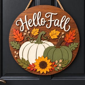 May include: A round wooden sign with a rope hanger featuring the text Hello Fall in white script. The design includes a large white pumpkin, a smaller green pumpkin, a bright yellow sunflower, and various orange, yellow, and green leaves.