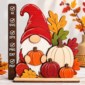 Peut inclure: Une décoration en bois représentant un gnome avec un chapeau rouge, une barbe blanche et plusieurs citrouilles orange, rouges et crème, agrémentée de feuilles d'automne. Un panneau vertical brun liste les formats AI, SVG, EPS, PNG, DXF et PDF.
