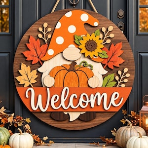 May include: A circular wooden door sign featuring a gnome with an orange polka-dot hat, holding a pumpkin. The sign is decorated with sunflowers and autumn leaves, with the word Welcome in white script on an orange banner across the center.