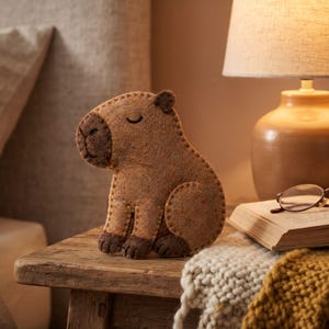 Cute capybara felt sewing project showing the finished stuffed animal ornament with warm golden-brown body, dark brown snout and peaceful sleepy expression.