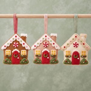 Finished brown felt gingerbread house ornament with white icing roof and chimney, red door, yellow windows, green bushes and wreath, colorful gumdrop details and hanging ribbon.