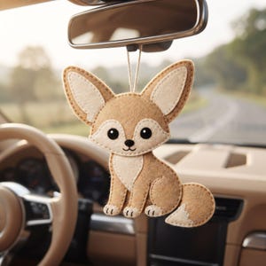 Close up of a handmade fennec fox ornament with large upright ears, cream face patch, black eyes and nose, and stitched smile.