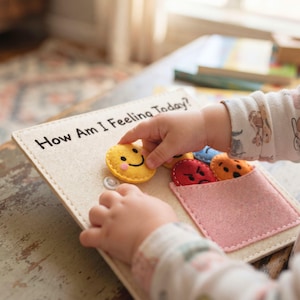 Toddler hands snapping felt happy face onto How Am I Feeling Today busy book page