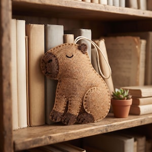 Finished handmade capybara ornament showing the rounded felt body, sleepy embroidered face, paws and hanging loop.
