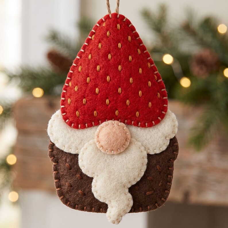 Handmade felt gnome ornament shown from another view with a red strawberry hat, cream beard, brown body, and decorative seed stitching.