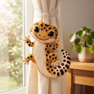 Handmade leopard gecko felt ornament with mustard yellow body, cream belly and feet, dark brown spots, large eyes, and a curled tail.