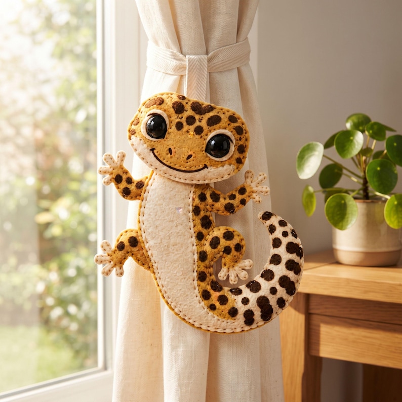 Handmade leopard gecko felt ornament with mustard yellow body, cream belly and feet, dark brown spots, large eyes, and a curled tail.