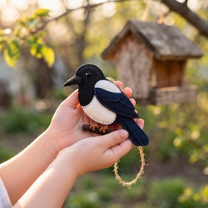 Child's hands holding a handmade felt magpie ornament in a garden
