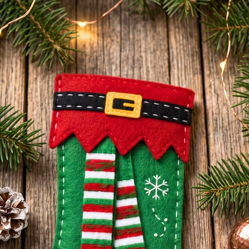 Close-up of a felt elf stocking ornament with black belt, gold buckle, red curled elf shoes, white cuffs and snowflake appliques.