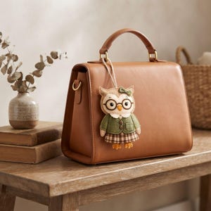 Cute handmade felt librarian owl ornament displayed upright, showing its round glasses, embroidered facial details, green cardigan, pocket, and plaid skirt.