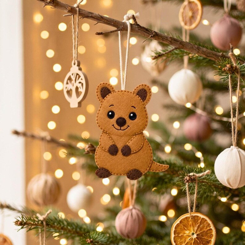 Cute handmade tan felt quokka ornament with rounded ears, dark brown details, smiling face, arms, feet, and curved tail on a light background.