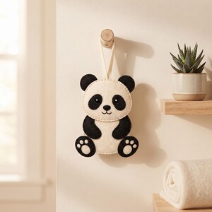 Handmade panda felt ornament hanging from a loop in a cozy home setting, showing the finished black and cream panda design.