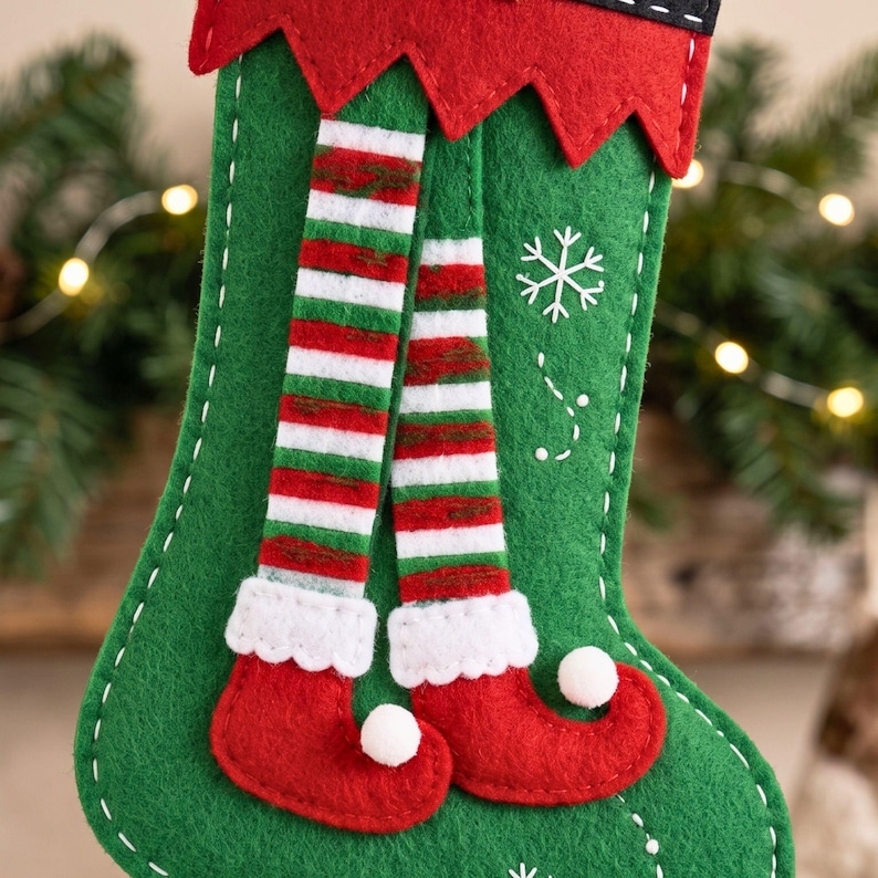 Handmade Christmas elf stocking showing the green stocking body, red cuff, striped elf legs, curled shoes, white cuffs and gold pom-poms.