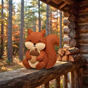 Felt squirrel with acorn ornament on a log cabin porch railing beside firewood