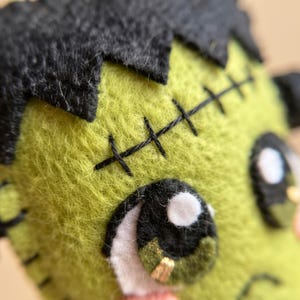 Close-up of hand stitching on a green felt Frankenstein ghost ornament showing the embroidered scar and blanket stitched edge.