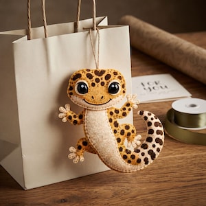Close view of a handmade felt leopard gecko showing the layered brown spots, cream eye rings, black eyes, small smile, and cream chin patch.