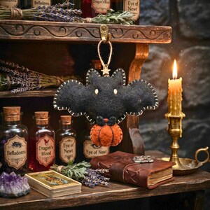 Black felt bat ornament perched on top of a glowing carved jack-o'-lantern at night