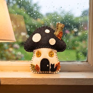 Felt mushroom house ornament on a rainy-day windowsill with droplets on glass
