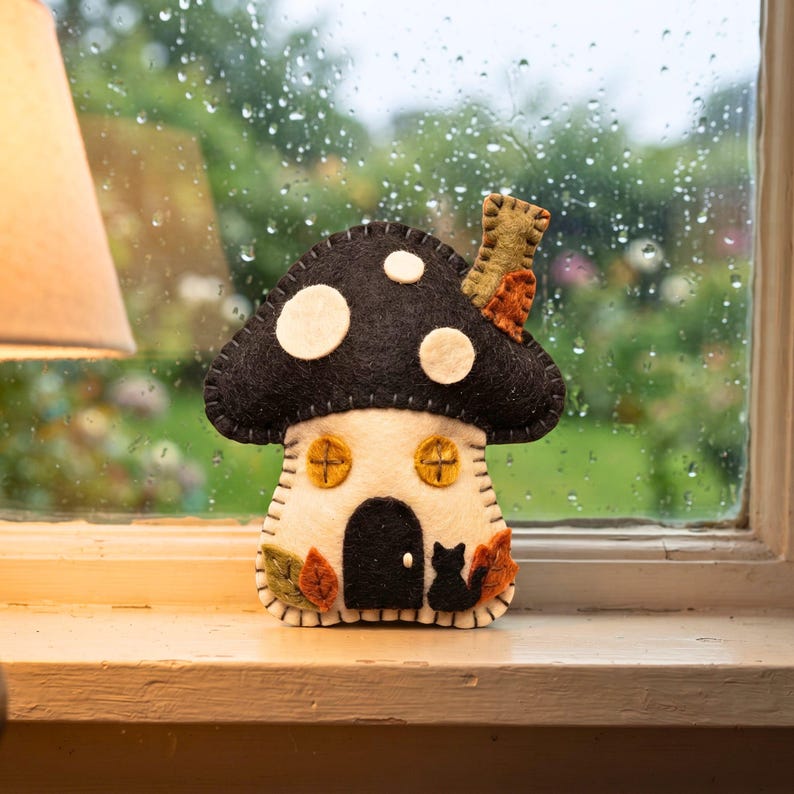 Felt mushroom house ornament on a rainy-day windowsill with droplets on glass