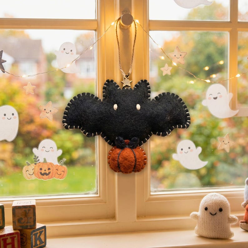 Black felt bat ornament with pumpkin hanging in a child's bedroom window with fairy lights