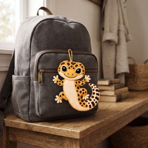 Cute leopard gecko ornament made from felt with a golden yellow body, dark brown leopard spots, cream details, and a hanging loop.