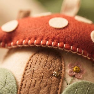 Felt mushroom house ornament styled on a wooden shelf next to vintage books and decor.