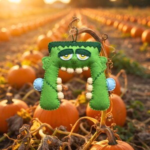 Green felt Frankenstein monster ornament hanging from a pumpkin vine in a pumpkin patch at golden hour.