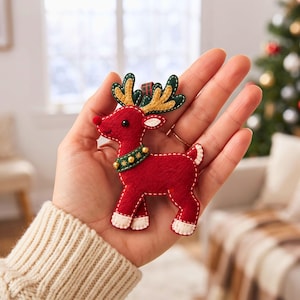 Finished stuffed felt reindeer ornament hanging from a red and green plaid ribbon with green antlers, cream hooves and gold jingle bells.