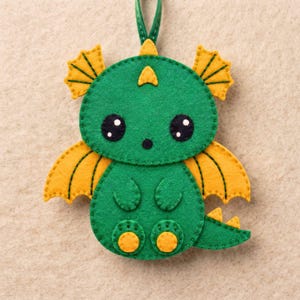 Close-up of a kawaii felt dragon face with black eyes and nose, white eye highlights, green felt head, decorative crest and golden-yellow wing details.