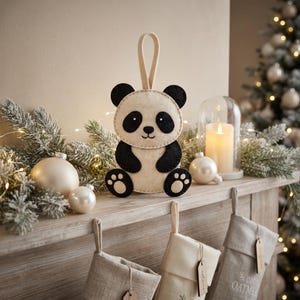 Cute finished felt panda ornament displayed in a warm home interior, showing the complete hand-sewn panda shape and hanging loop.