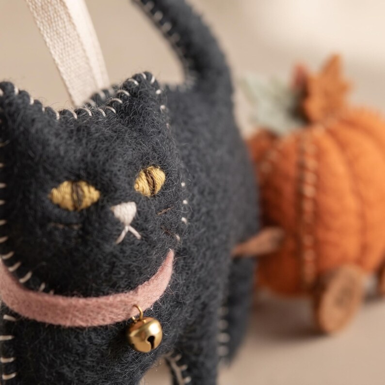 Crafter holding a handmade felt black cat ornament against a warm, neutral background.