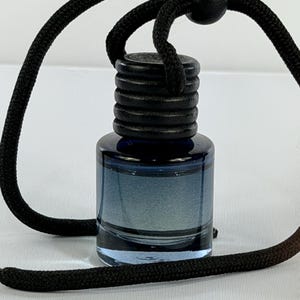 May include: A small, cylindrical glass bottle with a gradient blue tint, featuring a black ribbed wooden cap and a black adjustable cord with a round wooden bead, designed for hanging as an air freshener or decorative accessory.