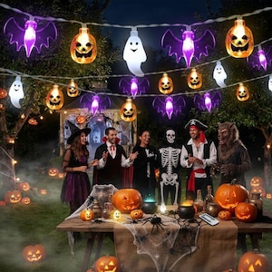 May include: A string of Halloween LED lights featuring purple bats, orange jack-o'-lanterns, and white ghosts. The lights are illuminated and hung in a festive outdoor setting, casting a glow over a table decorated with pumpkins and spiders.