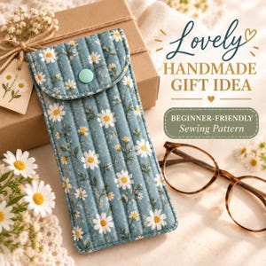 May include: A quilted fabric glasses case in a dusty blue color featuring a white daisy floral pattern, a mint green snap button closure, and vertical stitching. The text reads Lovely HANDMADE GIFT IDEA and BEGINNER-FRIENDLY Sewing Pattern.