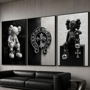 Op de afbeelding: Een set van drie wandkunstprints in zwart-wit. De buitenste panelen tonen een stripfiguur met X-vormige ogen zittend op een blok, terwijl het middelste paneel een metalen Chrome Hearts-kruisembleem bevat.