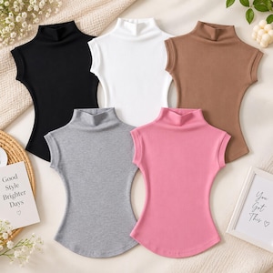 May include: A collection of five sleeveless mock neck tops in black, white, brown, gray, and pink. Each top features a fitted silhouette with a high neckline and cap sleeves. The garments are arranged in a cluster, showcasing the solid colors.