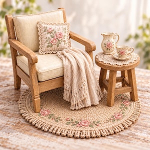 Puede incluir: Un sillón de madera en miniatura con cojín crema, una almohada cuadrada con rosas rosadas y una manta beige con flecos. Al lado hay un taburete de madera con una jarra y una taza de cerámica con motivos de rosas sobre un tapete de encaje.